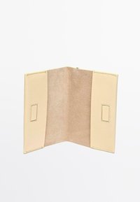 Beżowy skórzany portfel z miękkim wnętrzem i gładką fakturą. Posiada dwie przegrody oraz prostokątny metalowy akcent po każdej stronie.