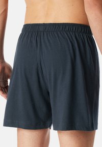 Shorts noirs en coton avec une taille élastique, offrant une coupe ample et un design simple. Texture lisse et coupe jusqu'aux genoux.