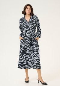 Abito a fantasia zebra in nero e grigio chiaro con bottone frontale, maniche lunghe e vita con cordoncino. Presenta tasche laterali e una lunghezza media.