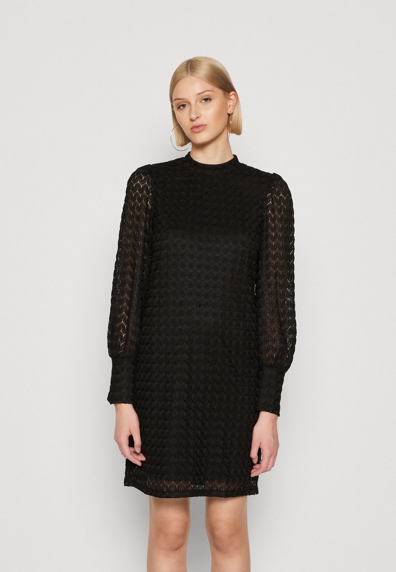 Vestido preto de renda com um decote alto, mangas longas transparentes e um padrão texturizado. Comprimento até o joelho com uma silhueta ajustada.