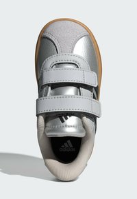 Strieborná športová topánka so syntetickou kožou a akcentmi z jemnej kože, vybavená dvoma suchými zipsami a gumenou podrážkou, vystavená zhora.