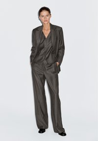Gray pinstriped suit with wide-leg trousers and a fitted vest, featuring a single-button blazer, sharp lapels, and a smooth texture.