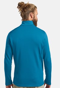 Pull bleu à manches longues avec un col haut, fabriqué à partir d'un tissu texturé, présentant une coupe ajustée et des accents contrastants aux épaules.
