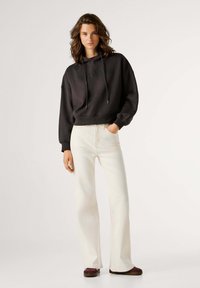 Felpa nera corta con coulisse, con testo sulla parte anteriore. Abbinata a jeans a gamba larga color crema chiaro e calzature scure.