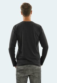 Black long-sleeve t-shirt made of cotton, featuring a round neckline and a straight fit, paired with gray jeans showing back pockets.