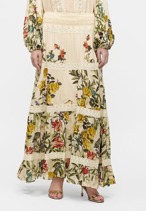 Lang cremefarvet kjole med farverige blomster- og fuglemønstre, blondebånd, lange puffede ærmer, kombineret med gyldne åbne højhælede sko.