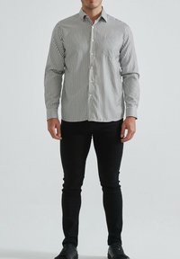 Chemise à rayures aux tons clairs et foncés, avec une poche poitrine, des manches longues et une coupe ajustée ; associée à un pantalon noir slim.