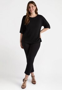 Musta löysä toppi puolihihalla, yhdistettyinä mustiin slim-fit-housuihin ja remmisandaaleihin. Pehmeä kangas, jossa on hienovarainen rakenne.