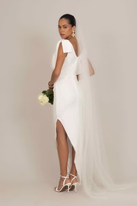 Weißes, enganliegendes Hochzeitskleid mit offener Rückseite, kurzen Ärmeln und hohem Schlitz. Kombiniert mit einem langen Schleier und einem hellfarbenen Rosenstrauß.