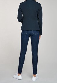 Blazer navy con spalle strutturate, abbinato a jeans scuri attillati e sneaker bianche. Linee pulite e design minimalista.