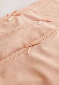 Beżowa bielizna z dekoracyjnymi brzoskwiniowymi kokardkami i zygzakowatym przeszyciem, charakteryzująca się gładką fakturą i bezszwowym wykonaniem.