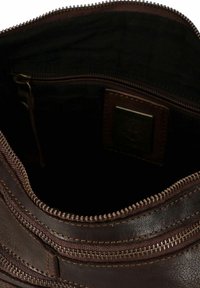 Interno di una borsa in pelle marrone con fodera nera. Presenta una chiusura con zip e una piccola tasca con una patch del logo. Materiale testurizzato e resistente.