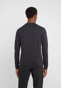 Maglione lavorato a maglia a maniche lunghe di colore grigio scuro con scollo rotondo e polsini a coste, indossato sopra pantaloni a quadri bianchi e neri.