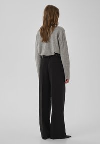 Grauer Strickpullover mit langen Ärmeln, kombiniert mit hoch taillierten, weit geschnittenen schwarzen Hosen. Das Outfit zeichnet sich durch minimalistisches Design und elegante Linien aus.