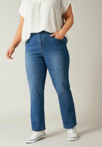 Siniset farkut, joissa on suora lahjetyyli, keskikorkea vyötärö, etutaskut ja hieman haalistunut viimeistely, yhdistettynä valkoiseen toppiin.