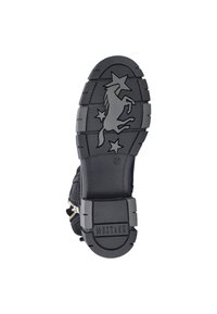 Semelle de botte en caoutchouc noir avec une surface texturée, présentant des motifs de cheval cabré et d'étoiles. Estampillé "MUSTANG" près du talon.