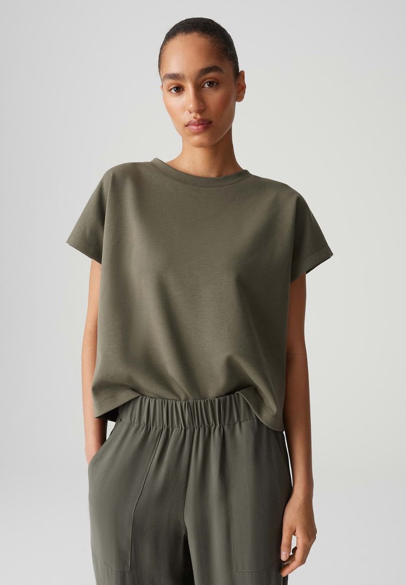 Olive green short-sleeve top with a round neckline, made of soft fabric, paired with matching elastic-waist trousers featuring side pockets.
