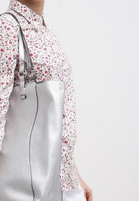 Söljskinn toteväska med texturerad yta, som har två axelremmar och en kontrasterande svart söm längs sidan.