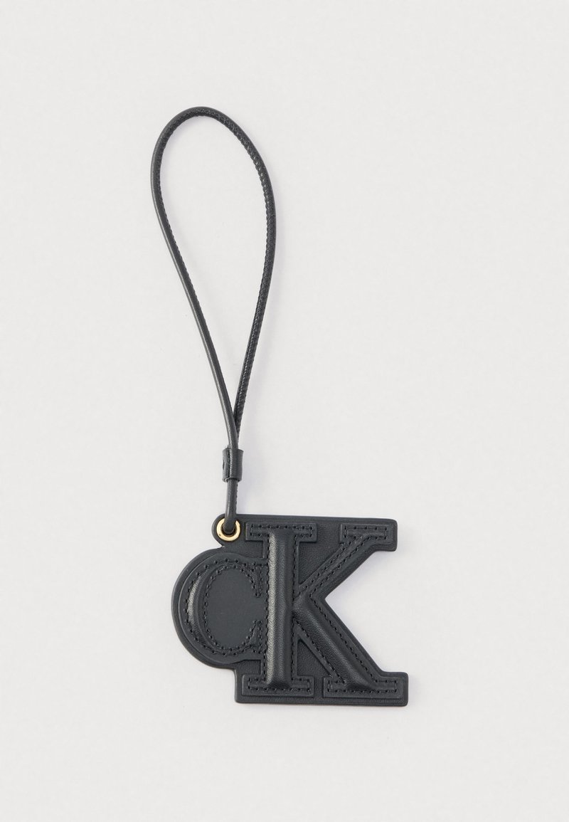 Porte-clés en cuir noir avec les lettres embossées "C" et "K" attaché à une sangle en boucle sur un fond blanc.