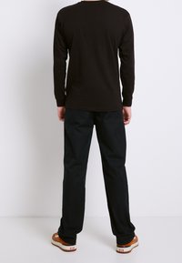 Maglietta nera a maniche lunghe con scollatura rotonda, abbinata a pantaloni neri larghi e sneakers marroni con suola bianca. Design semplice, senza motivi.