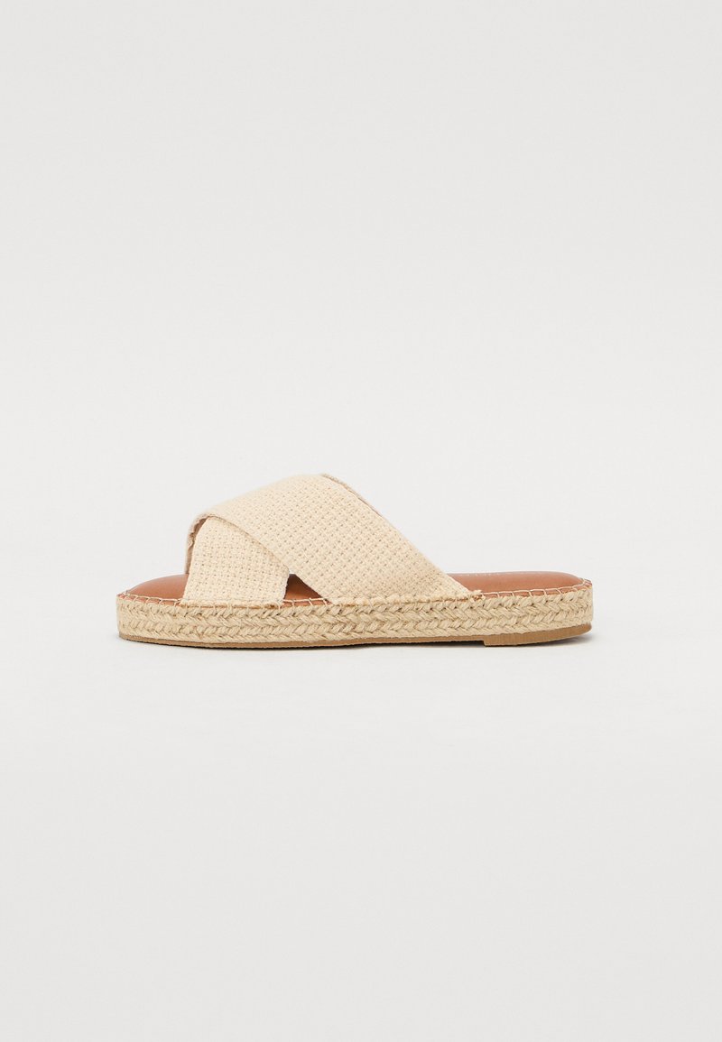 Beige kryssband sandaler med vevd tekstur, en flat såle innpakket i jute, og en glatt skinnsåle.
