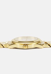 Orologio d'oro con cassa liscia, quadrante in vetro trasparente e cinturino elaborato con piccoli accenti di gemme. Corona posizionata sul lato destro.