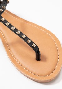 Infradito neri con cinturino texturizzato decorato da borchie a piramide argento e soletta in ecopelle beige.
