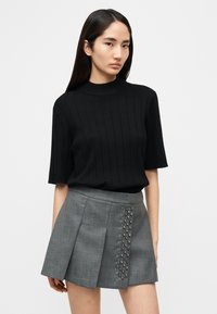 Μαύρο ριμπ πλεκτό τοπ με κοντά μανίκια συνδυασμένο με γκρι πλισέ φούστα που διαθέτει λαμπερά διακοσμητικά στη μία πλευρά.