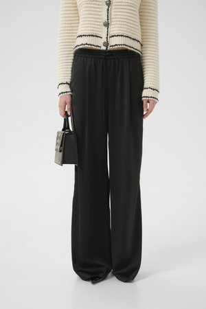 Black wide-leg trousers with a drawstring waist, styled with a textured cream cardigan and a small black handbag featuring metallic accents.