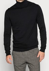 Schwarzer Rollkragenpullover aus weichem Strickstoff, mit taillierter Passform und geripptem Saum, kombiniert mit karierter grauer Hose.