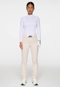 Pitkähihainen valkoinen istuva paita, beige räätälöidyt housut, musta vyö hopeisella soljella, valkoinen golf-käsine ja urheilulliset valkoiset kengät.