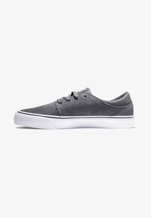 Zapatillas de ante gris con un diseño bajo y con cordones, suela de goma blanca y una franja negra en la base. Parte superior de tela texturizada.