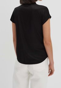 Top negro de manga corta con un dobladillo redondeado y textura suave; combinado con jeans blancos de pierna recta que son visibles en la parte inferior.