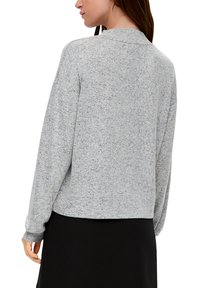 Szary, teksturowany sweter z długimi rękawami; głęboki dekolt w serek; luźny fason; noszony z czarną spódnicą; delikatne różnice w kolorze.