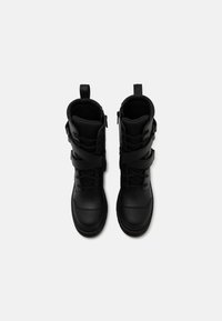 Bottines en cuir noir avec un laçage à l'avant, des zips sur les côtés et des accents de sangle. Finition texturée et bout renforcé.