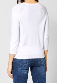 Bílý, lehký svetr s ¾ raglánovými rukávy, žebrovaným výstřihem a lemem. Doplněný modrými džínami s přiléhavým střihem a zadními kapsami.