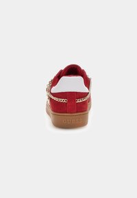 Sneakers en suede rouge avec des accents blancs et un détail en chaîne dorée sur le côté. Présente une semelle en caoutchouc marron et un talon avec logo.