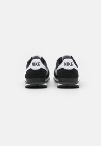 Sneakers Nike in bianco e nero con parte superiore in suede e mesh, con un marchio ben visibile sul tallone e suola in gomma texturizzata.