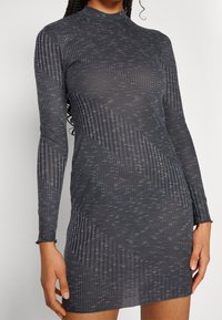 Robe grise à manches longues côtelée avec un col montant, un design ajusté et un motif texturé avec de subtiles variations de teinte.