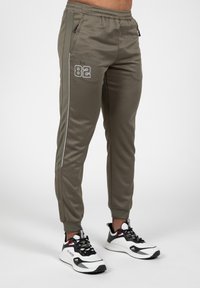 Slim-fit joggers in olijfgroen, met een elastische tailleband, zijzakken, witte accentstrepen en geprinte "Est. 82" detail.