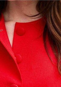 Roter Leinenjacke mit einem runden Kragen, zwei großen Knöpfen und einer glatten Textur, die ein sauberes und minimalistisches Design präsentiert.