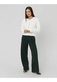 Cardigan blanc texturé avec un col rond et des boutons sur le devant, associé à un pantalon large vert foncé et des baskets vertes avec des accents roses.