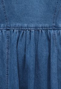 Détail d'un tissu en denim bleu avec une couture froncée et une couture verticale, montrant la texture et le motif de tissage.