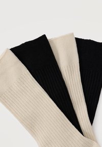 Δύο ζευγάρια ριμπ καλτσών, ένα μαύρο και ένα μπεζ, τοποθετημένα διαγώνια το ένα πάνω στο άλλο σε λευκό φόντο.