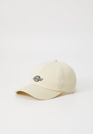 Casquette de baseball beige en tissu, avec une visière courbée et un patch logo noir à l'avant. Six œillets brodés pour la ventilation.
