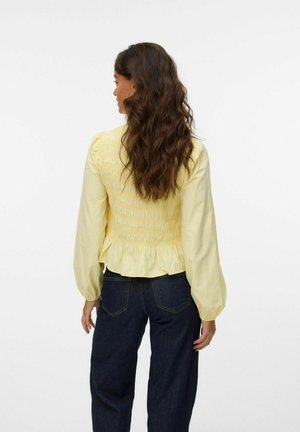 Kollane smock-kleidi pikade puff-särkidega ja frill-suudmega, mis on kombineeritud tumedate siniste teksadega. Sile kangas, millel on tekstuursed aktsendid taga.