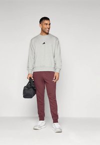 Γκρι φούτερ με μαύρο λογότυπο, βυσσινί παντελόνια φόρμας με λευκές ρίγες στο πλάι, λευκά αθλητικά παπούτσια και μαύρη τσάντα. Αθλητική καθημερινή εμφάνιση.