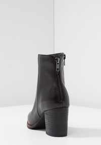 Botín de cuero negro hasta el tobillo con cremallera trasera, tacón apilado, textura suave y diseño sencillo. Presenta una puntera redondeada y costuras minimalistas.