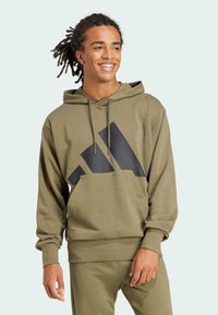 Olivgrön hoodie med en stor svart grafisk design, justerbar dragkedja på huvan, framficka i kängurustil och ribbade muddärmar.