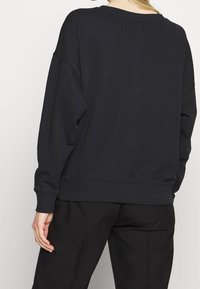 Sudadera negra de corte holgado, con hombros caídos, escote ancho, puños y dobladillo de canalé. Textura suave, sin patrones visibles ni herrajes.